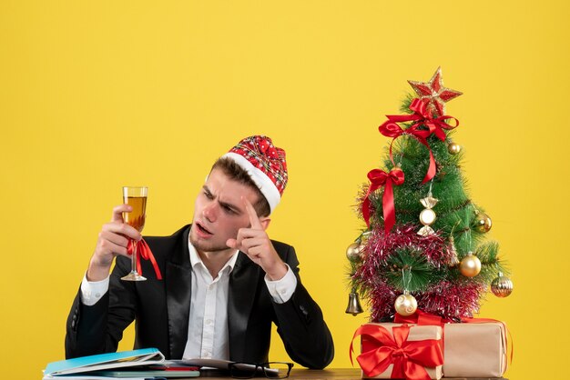 Operaio maschio di vista frontale che celebra natale con champagne intorno al piccolo albero di natale e regali su colore giallo