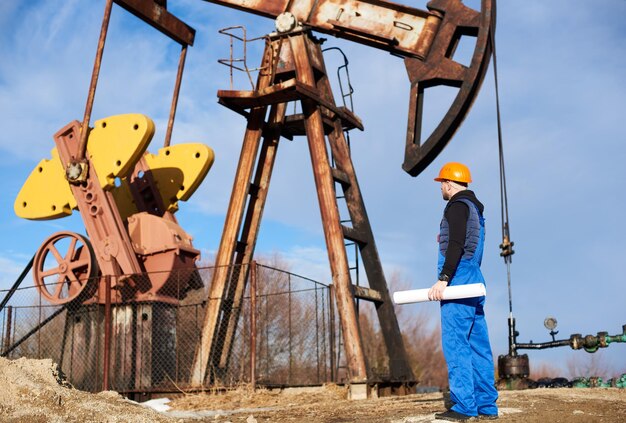Operaio petrolifero in piedi nel giacimento di petrolio accanto a un martinetto della pompa con una grande carta