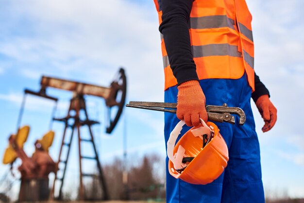 Operaio petrolifero in uniforme arancione e casco su sfondo il martinetto della pompa e il cielo blu