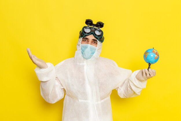 Operaio scientifico maschio di vista frontale in vestito speciale che tiene piccolo globo sulla superficie gialla