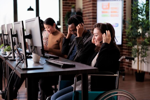 Operatore di assistenza clienti con condizioni di salute croniche che utilizzano sedia a rotelle in un ufficio adatto ai disabili. Donna che lavora presso l'helpdesk del servizio clienti del call center, che vive con disabilità fisiche.