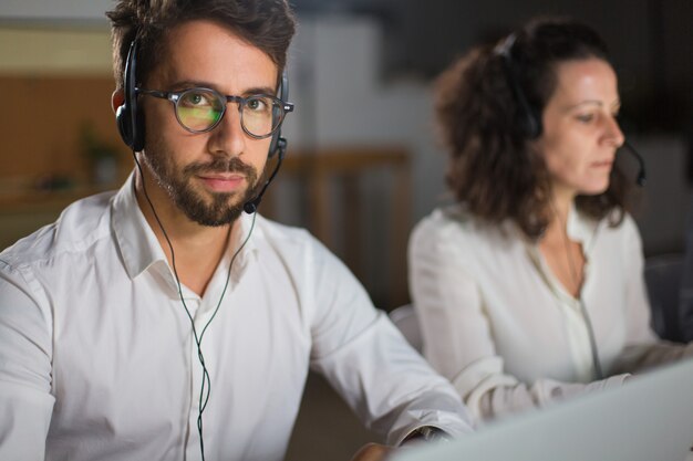 Operatore di call center bello in occhiali che guarda l'obbiettivo