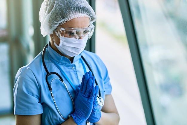 Operatore sanitario che prega con le mani giunte mentre lavora in ospedale