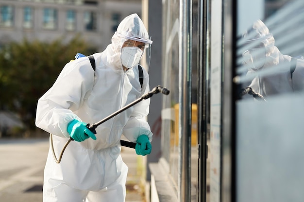 Operatore sanitario in tuta ignifuga che disinfetta l'edificio pubblico durante l'epidemia di coronavirus