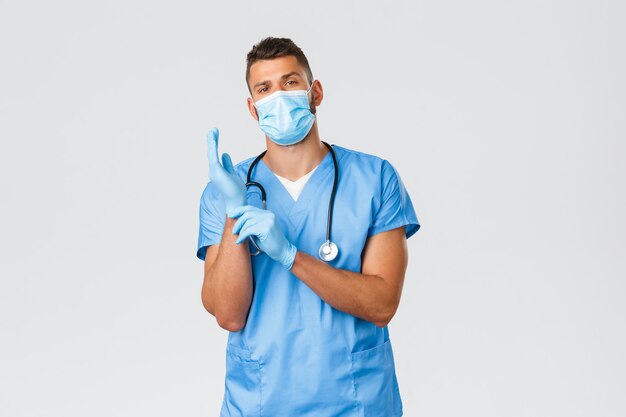 Operatori sanitari, covid-19, coronavirus e prevenzione del concetto di virus. Fiducioso medico maschio dall'aspetto serio, infermiere in maschera medica e scrub, indossare guanti per osservare il paziente in clinica.
