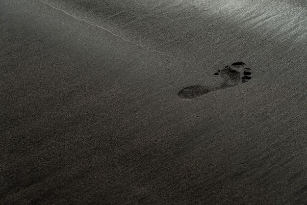 Orma su una macrofotografia nera della spiaggia di sabbia. Traccia umana su una trama setosa spiaggia nera con profondità di campo. Sfondo nero minimalista. Costa sabbiosa voulcanica di Tenerife.