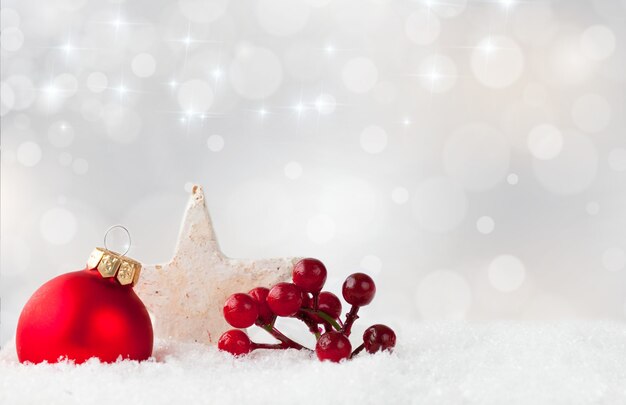 Ornamento di Natale rosso e bacche di arbusto di agrifoglio e una stella bianca su una superficie innevata