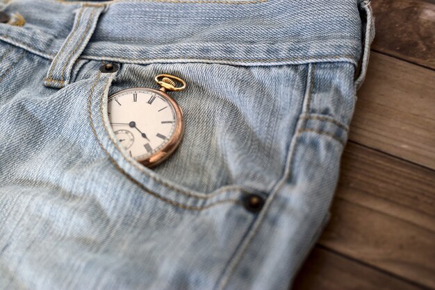 Orologio in una tasca dei jeans su una superficie di legno - concetto di gestione del tempo