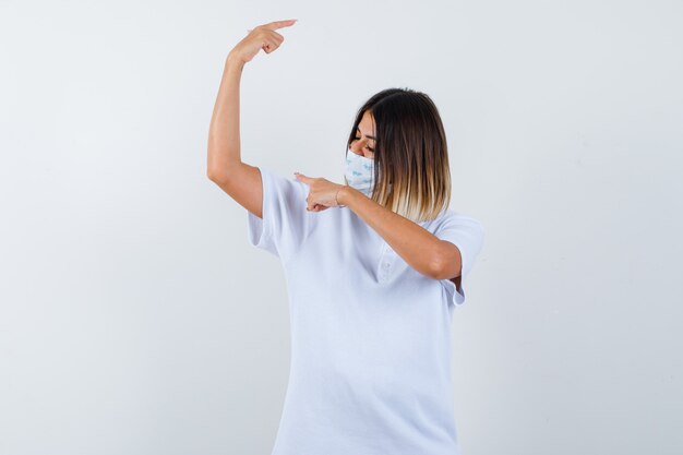 Ortrait di giovane donna che punta da parte in t-shirt, maschera e guardando fiducioso vista frontale