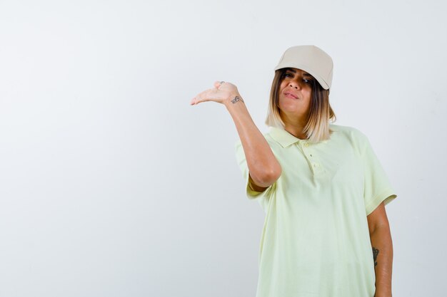 Ortrait di giovane donna che tiene qualcosa in t-shirt, berretto e che sembra vista frontale sicura