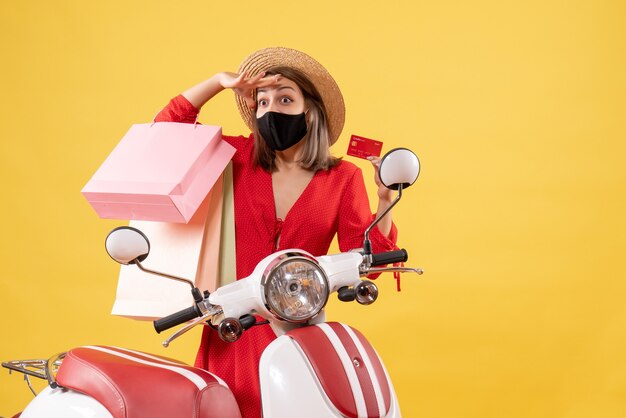 osservando la giovane donna con la maschera nera che tiene la carta di credito e le borse della spesa vicino al motorino