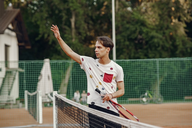 Ottima giornata per giocare! Allegro giovane uomo in maglietta. Ragazzo con racchetta da tennis e palla.