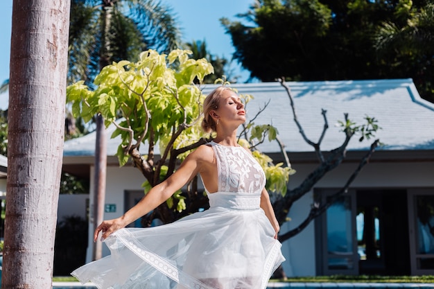 Outdoor ritratto di donna in abito da sposa bianco in villa in una giornata di sole, vista tropicale