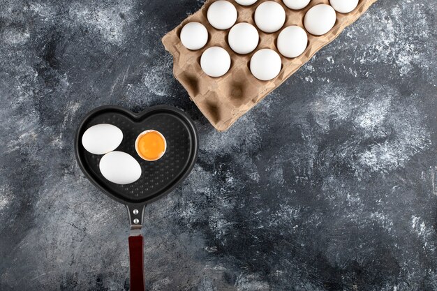 Padella e contenitore di uova sulla superficie in marmo.