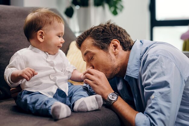 Padre affettuoso che bacia la mano del figlio del bambino mentre si diverte a tempo con lui a casa