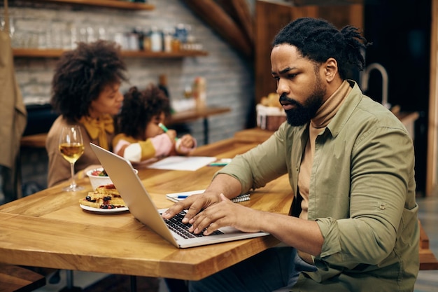 Padre afroamericano che lavora al computer portatile a casa