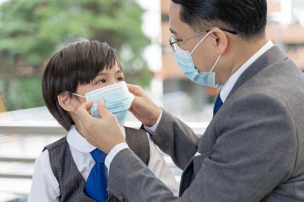 Padre che mette una maschera protettiva su suo figlio, famiglia asiatica che indossa una maschera per la protezione durante l'epidemia di Coronavirus covid 19 in quarantena