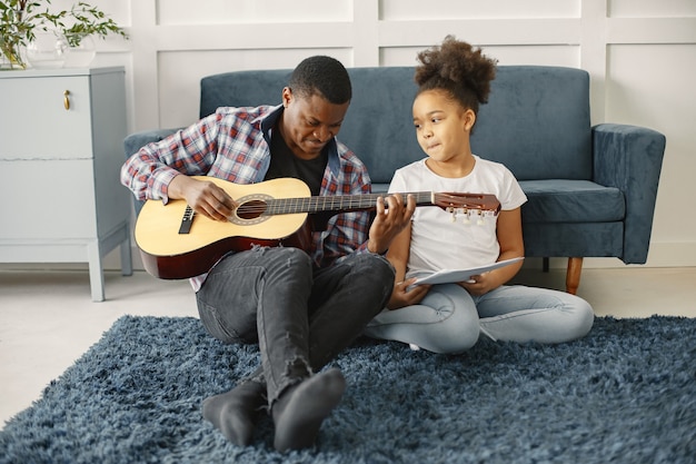 Padre con figlia sul divano. Ragazza che tiene una chitarra. Imparare la chitarra.