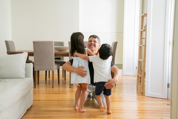 Padre di risata che abbraccia adorabili bambini piccoli a casa