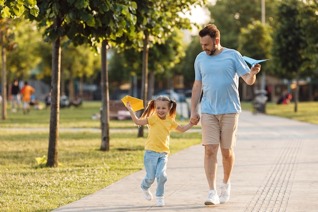 padre e figlia sorridenti emotivi con aerei di carta all'aperto