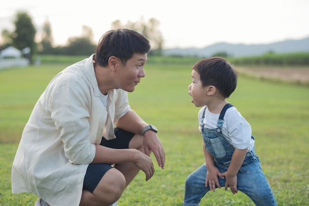 Padre e figlio che giocano nel parco all'ora del tramonto. gente che si diverte in campo. concetto di famiglia amichevole e di vacanza estiva. le gambe di padre e figlio camminano attraverso il prato nel parco