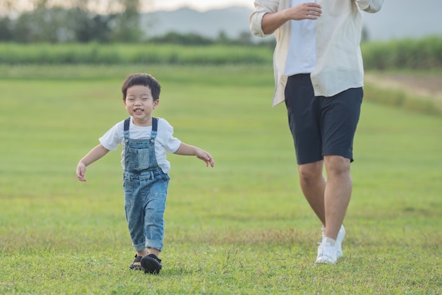 Padre e figlio che giocano nel parco all'ora del tramonto. gente che si diverte in campo. concetto di famiglia amichevole e di vacanza estiva. le gambe di padre e figlio camminano attraverso il prato nel parco