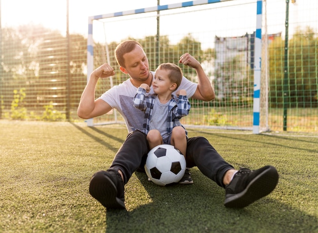 Padre e figlio che mostrano i muscoli sul campo di calcio