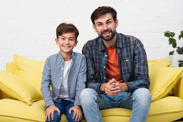 Padre e figlio seduti sul divano e guardando il fotografo