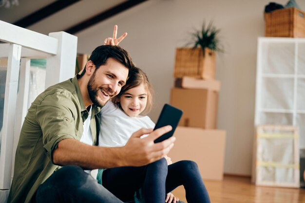 Padre felice che si fa selfie con la figlia giocosa nel loro nuovo appartamento