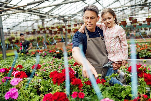 Padre felice che tiene la sua piccola figlia e le insegna il tipo di fiori mentre lavora al vivaio