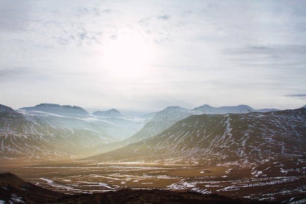 Paesaggio di colline coperte di erba e neve sotto un cielo nuvoloso e luce solare in Islanda