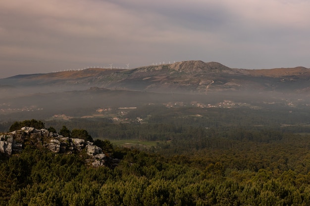 Paesaggio di colline e rocce ricoperte di vegetazione e nebbia sotto un cielo nuvoloso la sera