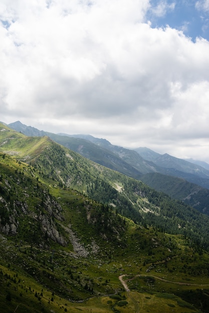 Paesaggio di colline ricoperte di vegetazione con montagne rocciose sotto un cielo nuvoloso