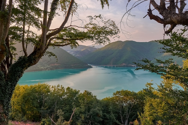 Paesaggio di mare circondato da colline ricoperte di verde sotto la luce del sole e un cielo nuvoloso