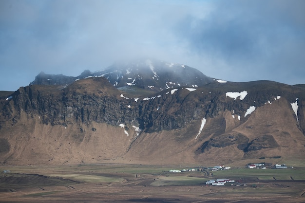 Paesaggio di montagne coperte di neve ed erba sotto un cielo nuvoloso in Islanda