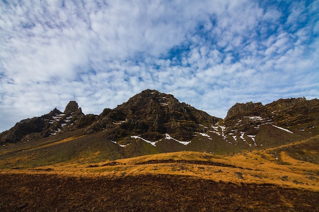 Paesaggio di rocce ricoperte di vegetazione e neve sotto un cielo nuvoloso in Islanda