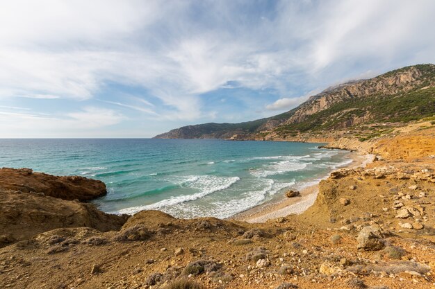Paesaggio di una costa pietrosa circondata da pianta sotto un cielo nuvoloso blu in Karpathos Grecia