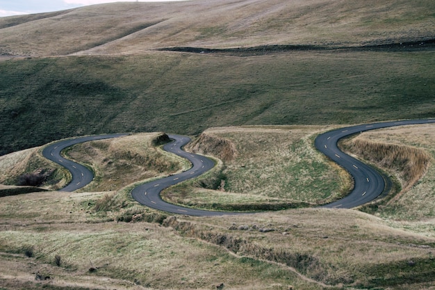 Paesaggio di una strada sinuosa circondata da colline ricoperte di erba durante il giorno