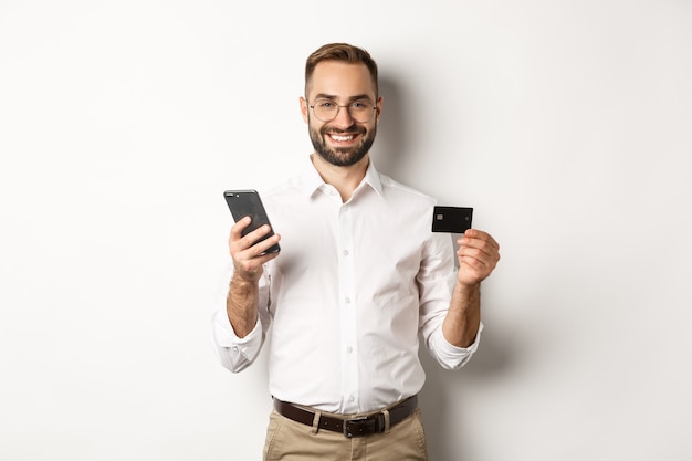 Pagamento aziendale e online. Sorridente imprenditore maschio shopping con carta di credito e telefono cellulare, in piedi