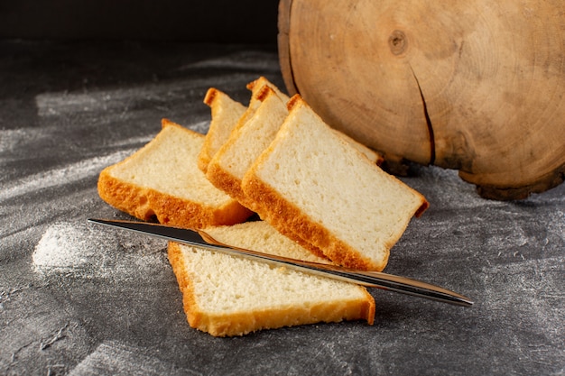 Pagnotte del pane bianco di vista vicina della parte anteriore affettate e saporito isolato con il coltello d'argento sulla superficie grigia