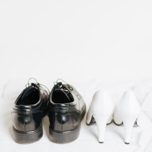 Paia dei tacchi alti di nozze e delle scarpe nere su fondo bianco
