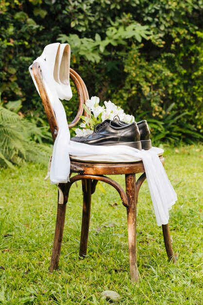 Paia dei tacchi alti e delle scarpe di nozze con il mazzo del fiore e della sciarpa su erba verde nel parco