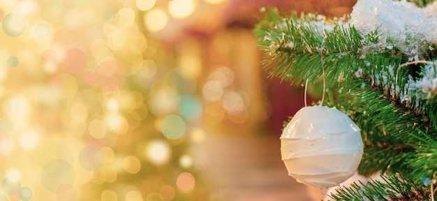 Palla di Natale bianca appesa a un ramo di abete innevato, sfondo effetto bokeh