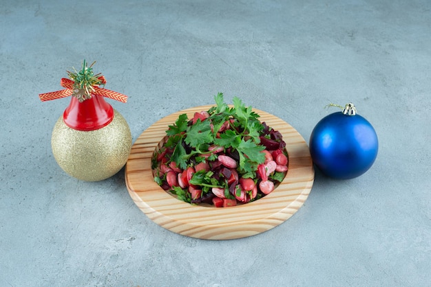 Palline di Natale accanto a un piatto di insalata di vinegret ricoperta di prezzemolo su marmo.