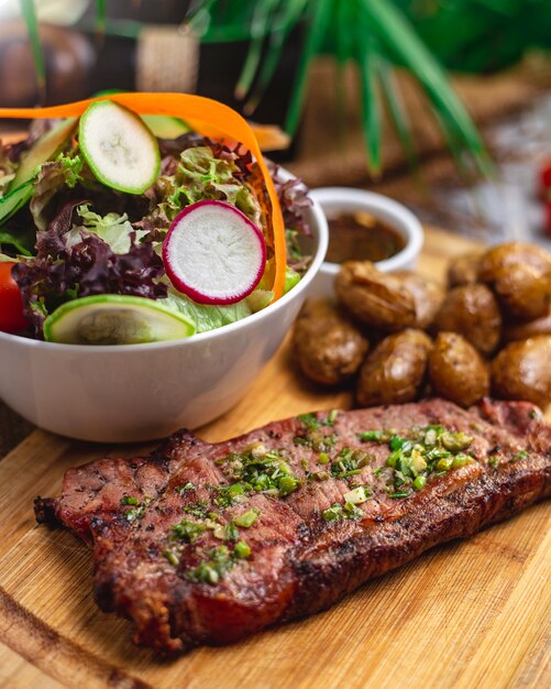 Palo di vista laterale con insalata di carne rossa alla griglia con verdure lattuga pomodoro ravanello cetriolo e patate arrosto sul tavolo