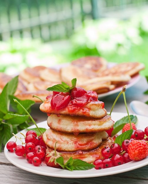 Pancake con le bacche su una tavola di legno in un giardino di estate