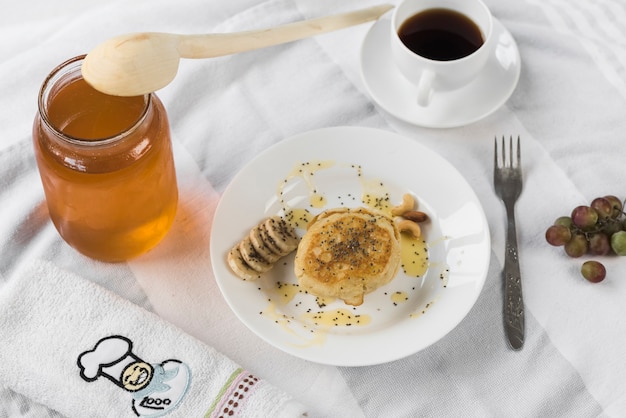 Pancake; con vasetto di miele; tazza di caffè sulla tovaglia