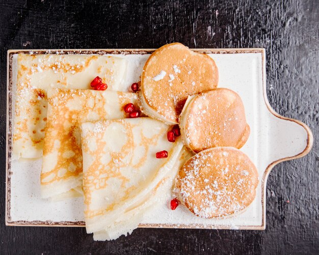 Pancake e crepes sul bordo di legno con zucchero in polvere e melograno sulla vista dall'alto