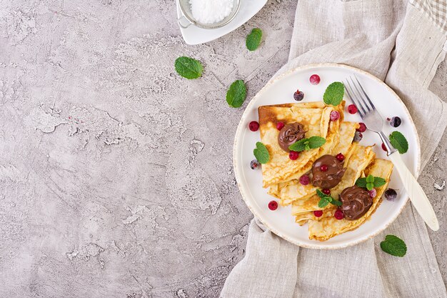 Pancakes con frutti di bosco e cioccolato decorati con foglie di menta. Gustosa colazione Vista dall'alto