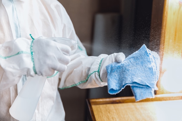 Pandemia di coronavirus. disinfettante in tuta protettiva e maschera spruzza disinfettanti in casa o in ufficio